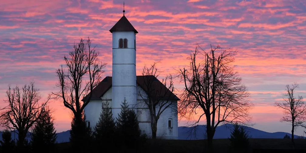 Cerkev svetega Volbenka v Zelšah, fotografirana ob sončnem zahodu, nebo nad njo je okrašeno s prelepimi vijoličastimi odtenki.