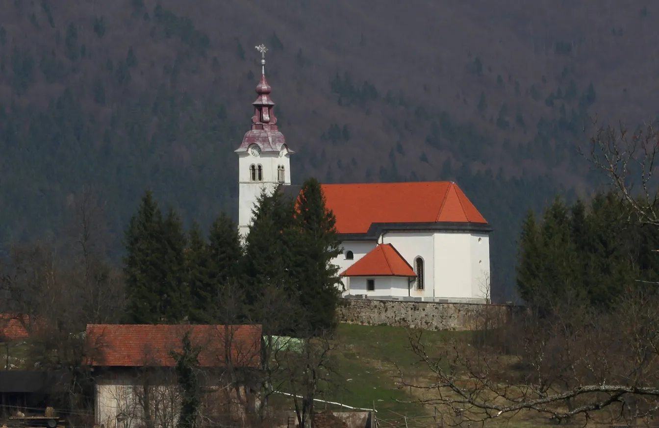 Cerkev sv. Pavla v vasi Žerovnica z oranžno streho, rdečkastim zvonikom in nizkim kamnitim zidom okoli nje, stoječa na hribu.